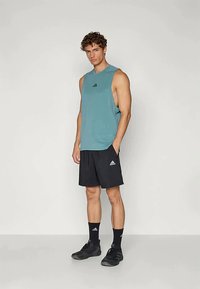 Világoskék ujjatlan sportpóló, fekete rövidnadrág, fekete sportcipő és zoknik. Az Adidas logó mind a pólón, mind a rövidnadrágon megtalálható.