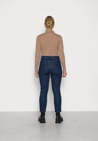 Hnědý žebrovaný dlouhý rukáv top zasunutý do tmavě modrých vysokých džín, doplněný černými kotníkovými botami, pohled zezadu.