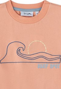 Pfirsichfarbene T-Shirt mit geripptem Ausschnitt, verziert mit blauen Wellen- und Sonnenstickereien sowie dem Text "SURF SPOT" in hellblau. Weicher Stoff.