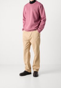 Felpa rosa di cotone con scollo rotondo, pantaloni beige e scarpe nere in pelle. Presenta un logo sul petto e una vestibilità comoda.