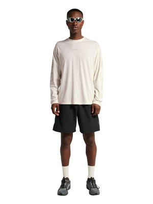 Mężczyzna ubrany w białą koszulę z długim rękawem z napisem, czarne spodenki, białe skarpetki, szare sneakersy i białe okulary przeciwsłoneczne, stojący na białym tle.