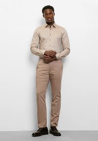 Light beige button-up shirt with collar, paired with matching beige trousers. The outfit features a slim fit and smooth texture, complemented by dark shoes.
