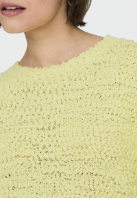 Maglione giallo lavorato a maglia con un motivo testurizzato e un ampio scollo rotondo. Il materiale sembra leggero e leggermente aderente.