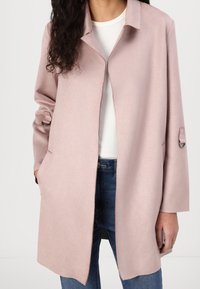 Light pink, mid-length coat made of soft fabric; features a collar, open front, and side pockets; has rolled sleeves with button accents.