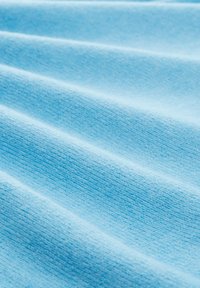 Ljusblått tyg med en mjuk, texturerad yta; har subtila, jämna vågor och en slät finish; lämpligt för kläder eller stoppning.