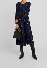 Navy sukienka w kwiaty z długimi rękawami, ozdobiona pomarańczowymi i niebieskimi kwiatami. Połączona z czarną, strukturalną torebką oraz czarnymi wysokimi botkami.