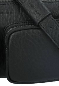Borsa in pelle nera con superficie texturizzata, scomparti con zip e tracolla. Dettaglio del marchio impressa di nota.