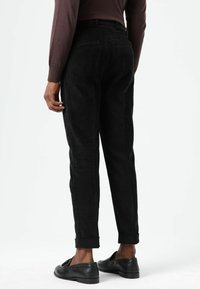 Zwarte corduroybroek met taps toelopende pijpen en opgerolde manchetten, voorzien van een getextureerd oppervlak en zijzakken. Gecombineerd met zwarte loafers.