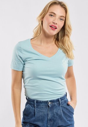 T-shirt léger bleu clair à manches courtes et col en V, fabriqué en tissu doux, présentant un petit motif floral sur la poitrine gauche.
