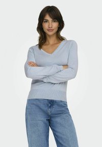 Maglione a V blu chiaro in morbido tessuto a maglia con maniche lunghe e orlo a costine fitted, abbinato a jeans in denim blu chiaro.