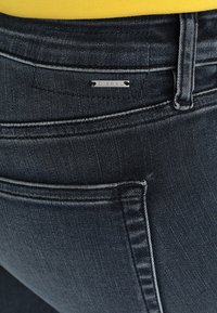 Jeans de mezclilla oscura con una textura suave, que presentan un contraste de costuras claras, una pequeña etiqueta de metal con el logo y bolsillos traseros estándar.