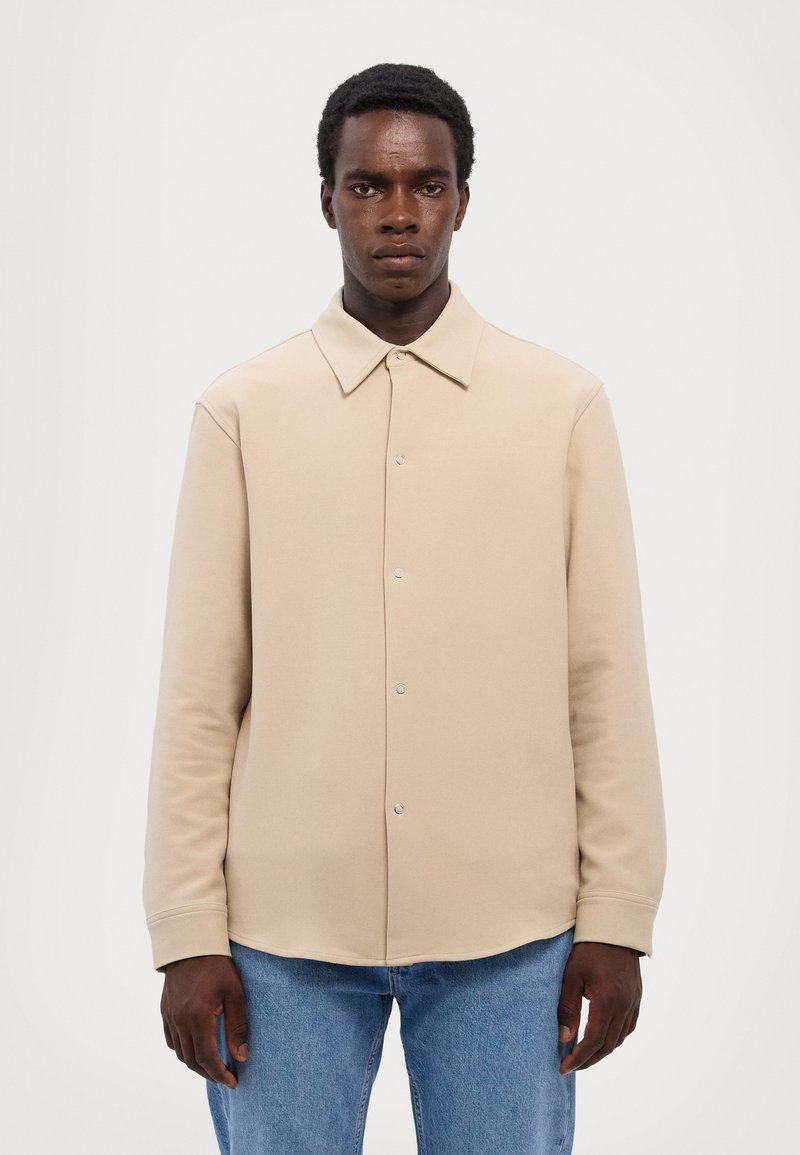 Beige overhemd met knopen en een spread collar, lange mouwen, een gladde textuur en een gebogen zoom. Gecombineerd met blauwe spijkerbroek.