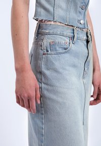 Ljusblå denimkjol med hög midja, dragkedja fram och fransade kanter. Tyget har en blekt struktur med subtila sy detaljer.