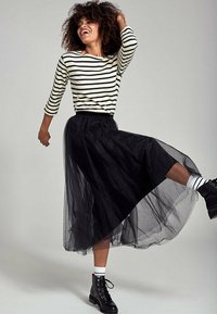 Zwarte tule midi-rok met een elastische tailleband, gecombineerd met een gestreept shirt met lange mouwen en zwarte veterschoenen.