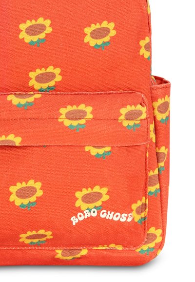 Sac à dos en tissu orange avec un motif de tournesols, comportant une poche à l'avant et le nom de la marque "Bobo Choses" en lettres blanches.