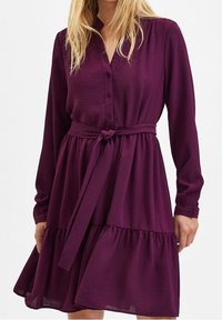 Lila långärmad klänning med knappstängning framtill, bälte i midjan och lägre kjol, tillverkad av ett texturerat, lätt tyg.