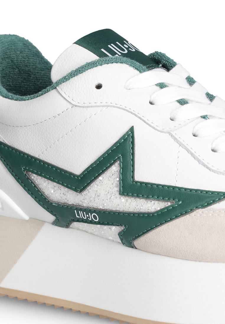 Zapatilla blanca con detalle en forma de estrella verde, forro interior verde texturizado, cordones blancos, punta de gamuza beige y suela blanca gruesa con banda de rodadura beige.