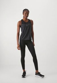 Μαύρο αμάνικο αθλητικό τοπ με υφασμάτινο μοτίβο και λογότυπο, σε συνδυασμό με εφαρμοστά μαύρα κολάν και αθλητικά παπούτσια.