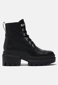 Bottes de cheville en cuir noir avec semelle épaisse à plateforme, œillets en métal et design à lacets. Présente un patch logo sur le côté et des accents texturés.