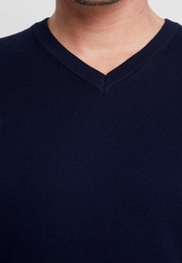 Marinblå v-ringad tröja i ribbat stickat tyg, med en texturerad yta och en djup ringning. Närbild av materialet.