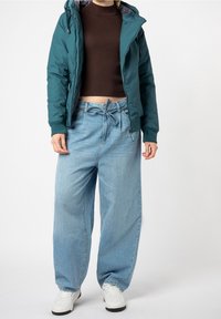 Tyrkysová puffer bunda, zipováním vpředu, elastické manžety; hnědý žebrovaný crop top; světle modré široké džíny s tkaničkami; bílé tenisky.