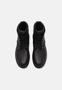 Stivaletti neri con lacci, realizzati in pelle texture, dotati di un colletto imbottito, lacci piatti e una punta rotonda.