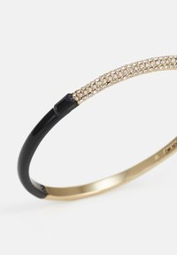 Juodas ir auksinis apyrankės bangles, turintis tekstūruotą juostą su auksinės spalvos blizgučiais ir blizgiai juoda dalimi sagtelių.