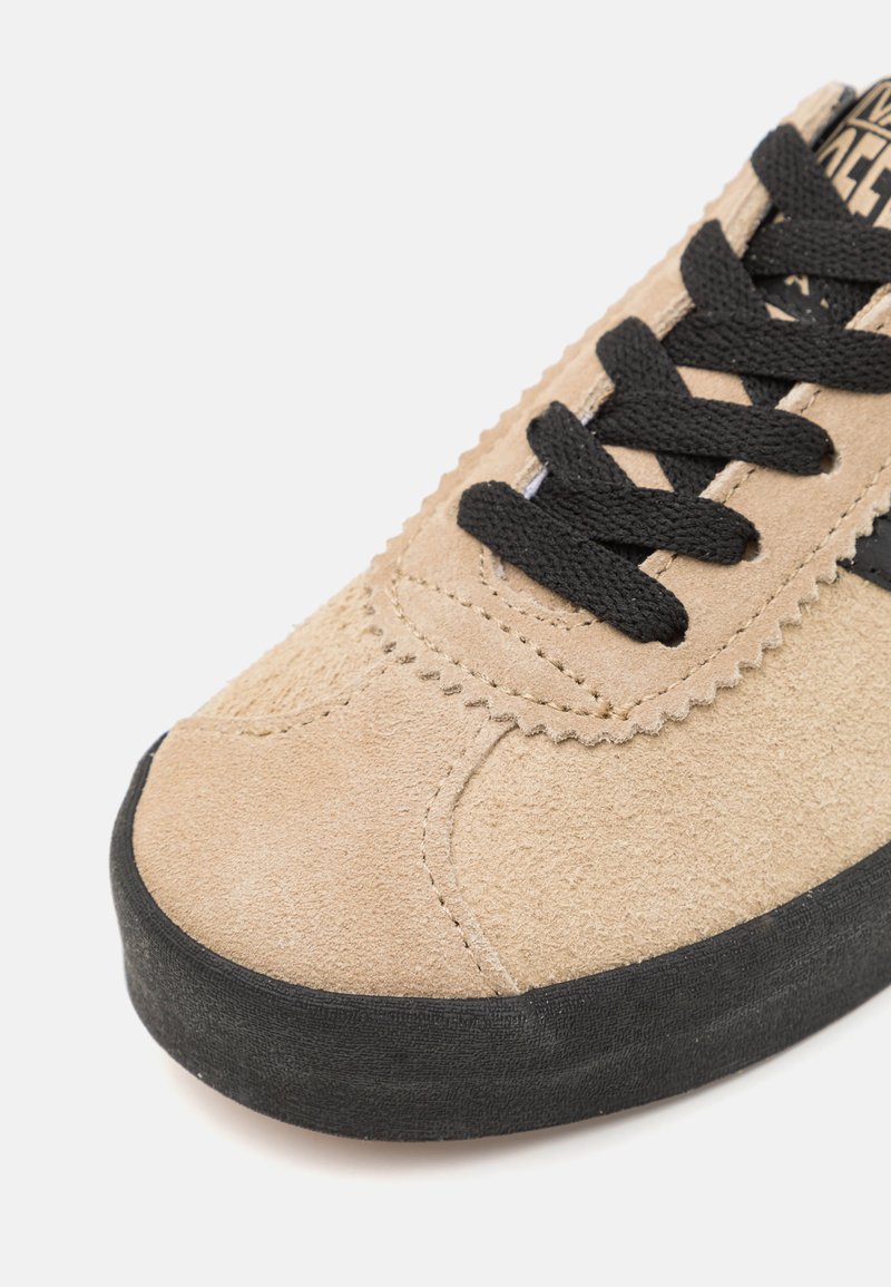 Beige Wildlederschuhe mit schwarzen Schnürsenkeln und einer Gummisohle. Mit gewelltem Rand und Steppdetails an den Seiten.