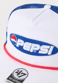 Λευκό καπέλο με μπλε διάτρητη πλάτη, με μεγάλο μπλε και κόκκινο λογότυπο Pepsi. Κόκκινη πλεγμένη διακόσμηση μπροστά, με μια μαύρη ετικέτα στο πλάι.