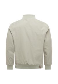 Vaaleabeige takki nähdään takaa, jossa on resorikaulus, hihansuut ja vyötärönauha sekä pieni ruskea kangastuppi lähellä alahelmaa.