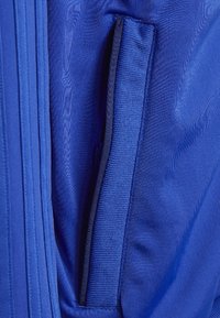 Modrá látka s hladkou texturou má boční kapsu. Design zahrnuje vertikální švy podél okrajů.