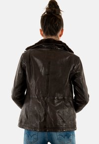 Veste en cuir marron avec col en fausse fourrure, coupe ajustée, coutures visibles et patch de marque rectangulaire à l'arrière.