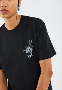 Svarte bomull t-skjorte med en hvit grafikk av en takeaway-beholder med nudler og spisepinner, med teksten "Yokohama Chinatown" under.