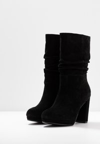Black suede ankle boots with a slouched design, rounded toe, and a high block heel. Smooth texture with no visible hardware or accents.