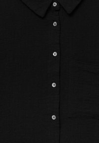 Chemise noire boutonnée en tissu texturé avec un col, dotée de boutons argentés et d'une poche poitrine pour un usage pratique.