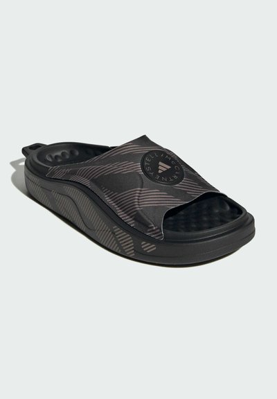 Black slide sandal with textured strap and grooved footbed. Features a round logo on the strap and diagonal stripes on the side.
