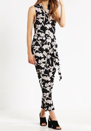 Kombinezon w kwiaty w kolorze czarnym i kremowym, bez rękawów, z kopertowym krojem i paskiem do wiązania. Połączony z czarnymi szpilkami, o dopasowanym kroju i długości do kostek.