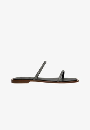 Sandales plates en cuir noir avec de fines lanières ornées d'accents métalliques décoratifs et une semelle intérieure texturée ; design minimaliste avec une semelle plate.