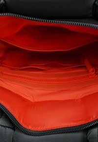 Interno di una borsa nera con due scomparti. Fodera rossa vivace, texture liscia, tasca con zip visibile e dettagli di cuciture rinforzate.