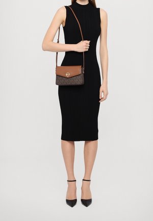 Robe noire côtelée associée à un sac bandoulière marron à monogramme avec un logo doré, accompagnée de talons noirs à bout pointu.