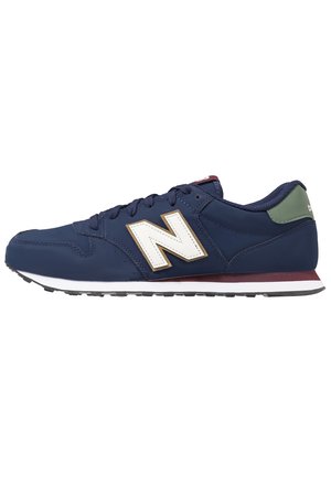Marineblå New Balance-sneaker med hvidt "N"-logo, vinrød midtersålstribe, grøn hælfane og sort mønstret ydersål.