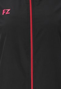 Svart jacka med en centrerad röd dragkedja och rosa "FZ"-logotyp på vänster bröst.