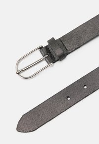 Musta kangasvyö, jossa on teksturoitu muotoilu, hopeanvärinen metallisolki ja useita säätöaukkoja. Tasaiset reunat ja teräväkärkinen pää.