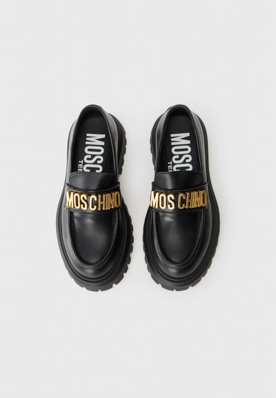 Svarta läder loafers med en kraftig gummisula och en gold "MOSCHINO" märkesrem över framsidan, med en rundad tådesign.