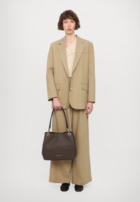 Blazer oversize beige e pantaloni a gamba larga con un top beige texture. Borsa nera con dettagli marroni a fantasia e accenti dorati.