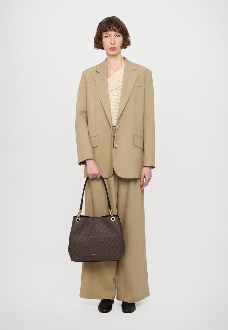 Blazer oversize beige e pantaloni a gamba larga con un top beige texture. Borsa nera con dettagli marroni a fantasia e accenti dorati.