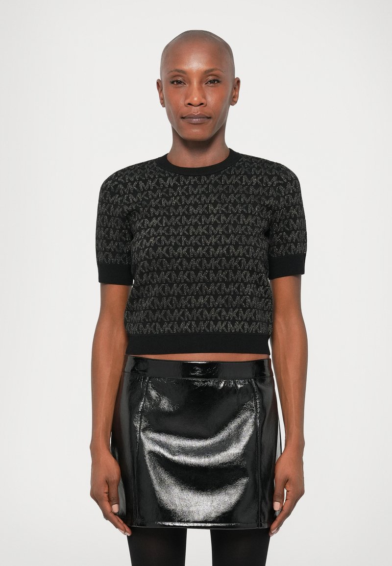 Maglione cropped nero con maniche corte caratterizzato da un motivo testurizzato. Abbinato a una mini gonna nera lucida. Entrambi presentano un aspetto elegante.