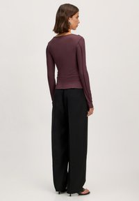 Slim-fit, lange mouw top in donkerpaarse geribbelde stof, gecombineerd met losse, zwarte wijde broek. Gedetailleerde naden en subtiele texturen zijn zichtbaar.