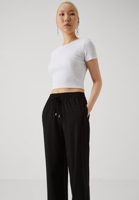 Un haut court côtelé blanc associé à un pantalon de jogging noir à taille élastique. Les pantalons de jogging disposent de poches latérales et d'un cordon de serrage avec des embouts en argent. Texture lisse.