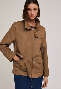 Brązowa bawełniana kurtka z wysokim kołnierzem, zatrzaskami i dwiema przednimi kieszeniami; gładka faktura z wyraźnie zarysowanym krojem.